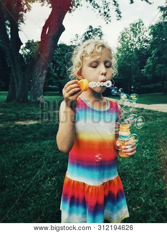 Candid Portrait Of Funny Little Blonde Caucasian Child Girl Blowing Soap Bubbles In Park At Summer S