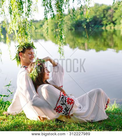 Midsummer. Young Loving Couple In Slavic Costumes On The Shore Of The Lake. Slavonic Holiday Of Ivan