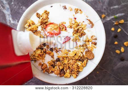 Muesli With Chocolate And Fresh Strawberries On A Dark Gray Background. Milk Is Poured Into The Plat