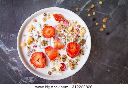 Muesli With Chocolate And Fresh Strawberries With Milk In A Plate On A Dark Gray Background. The Con