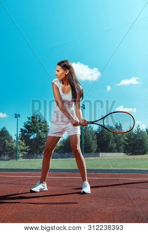 Slim And Fit Dark-haired Woman Holding Racket Training On Court