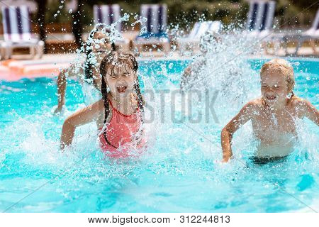 Children Laughing While Splashing Water In Swimming Pool