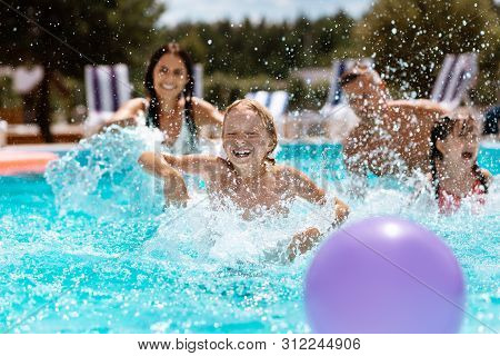 Parents And Children Laughing While Playing Ball In Swimming Pool
