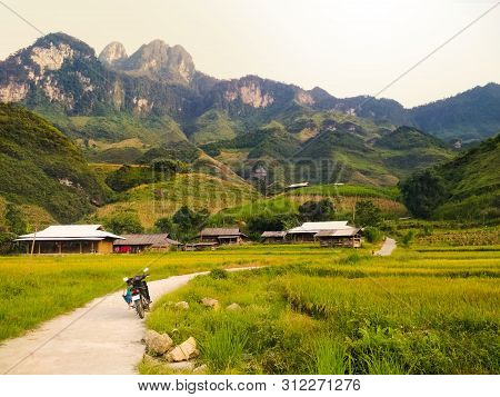 Motorbike Parked Next To Bright Green Rice Fields Surrounded By Local Village And High Mountains. Tr