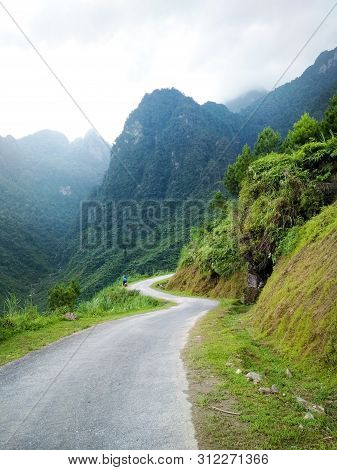 Curved Road Surrounded By High Blue Mountains With Lonely Motorbike In The Distance. Beautiful Views
