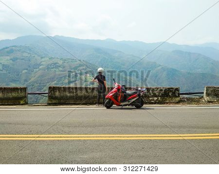 Girl In A Helmet With Her Red Scooter Parked On A Side Road Enjoying Beautiful View Of High Mountain