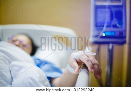 Selective Focus To Hand Of Patient Draw To Infusion Pumps And Saline Bag In Hospital. Blurry Infusio