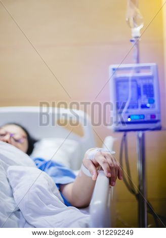 Selective Focus To Hand Of Patient Draw To Infusion Pumps And Saline Bag In Hospital. Blurry Infusio
