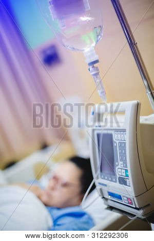 Selective Focus To Hand Of Patient Draw To Infusion Pumps And Saline Bag In Hospital. Blurry Infusio