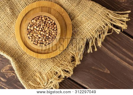 Lot Of Whole Raw Brown Buckwheat Grain In A Wooden Bowl On Bamboo Plate On Jute Cloth Flatlay On Bro