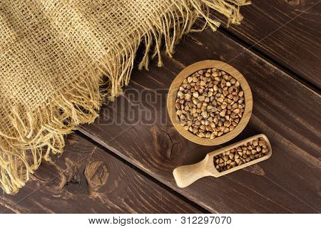 Lot Of Whole Raw Brown Buckwheat Grains In A Wooden Bowl And A Scoop With A Piece Of Jute Cloth Flat