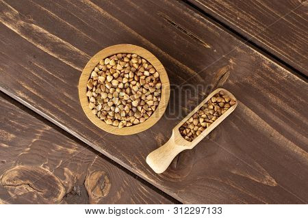 Lot Of Whole Common Raw Brown Buckwheat Grain In A Wooden Bowl With Wooden Scoop Flatlay On Brown Wo