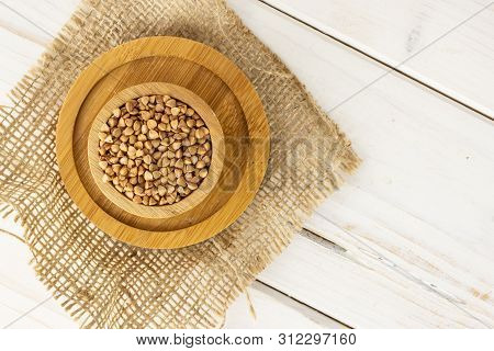 Lot Of Whole Raw Brown Buckwheat Grain In A Wooden Bowl On Jute Cloth On Bamboo Plate Flatlay On Whi