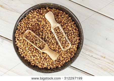 Lot Of Whole Raw Brown Buckwheat Grain In A Grey Ceramic Bowl With Wooden Scoop Flatlay On White Woo