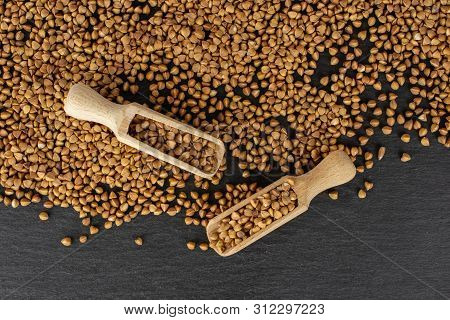 Lot Of Whole Raw Brown Buckwheat Grain Two With Wooden Scoop Flatlay On Grey Stone
