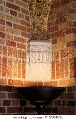 June 29, 2019 In Eugene, Or:  Lamp Shinning Light On A Decorative Religious Cross Besides A Brick Wa