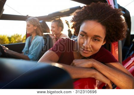 Millennial African American woman on road trip with friends, leaning out of the car window, close up