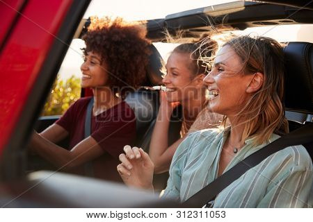 Three millennial female friends on a road trip driving together in an open jeep, close up