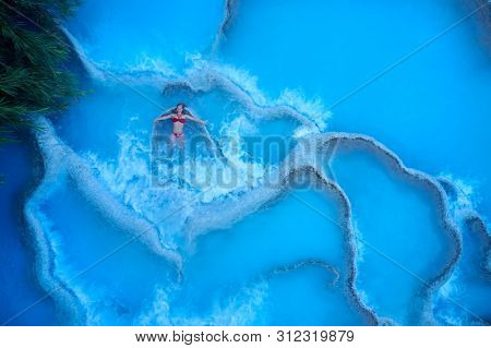 young woman relaxing at natural spa with waterfalls and hot springs at Saturnia thermal baths, Grosseto, Tuscany, Italy