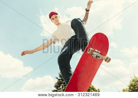 Skateboarder Doing A Trick At The Citys Street In Sunny Day. Young Man In Sneakers And Cap Riding An