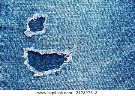 Textured denim background. Torn hole in the fabric. Blue tones