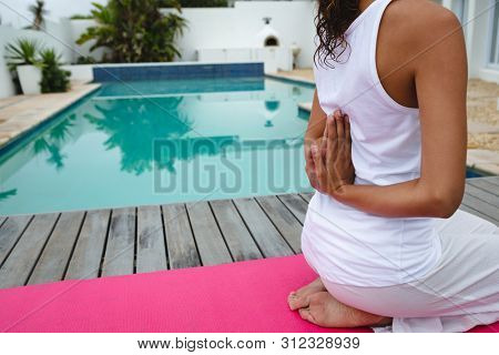 Close-up of mixed-race woman performing yoga near swimming pool in the backyard. Summer fun at home by the swimming pool