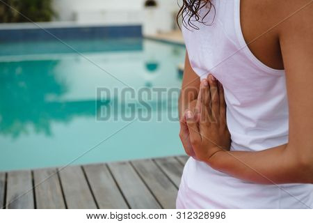 Mid section of mixed-race woman performing yoga near swimming pool in the backyard. Summer fun at home by the swimming pool