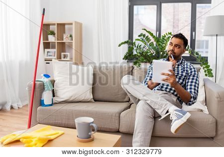 household and time management concept - indian man making to do list in notebook after home cleaning