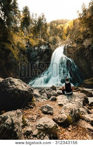 Single Man Sitting Near Gollinger Waterfall In Austria. Travel Summer Alps Concept.