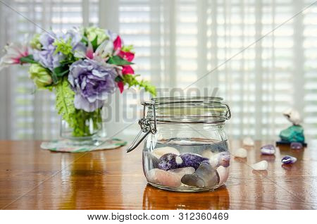 Combination of amethyst, rose quartz and blue lace agate making gem elixir in a glass jar on a table. Stones create highly vibrational water that captures the gemstone meanings and healing properties.