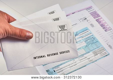 Human Holds In Hand Three Mails From The Internal Revenue Service Next To 1040, Schedule D Form 1040