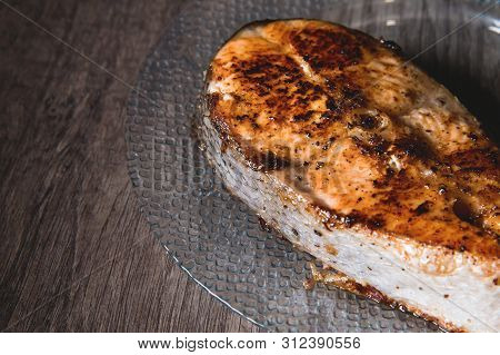 Close-up One Grilled Cum Salmon Keta Fish Steak On A Glass Transparent Plate On A Dark Wood Table Ba