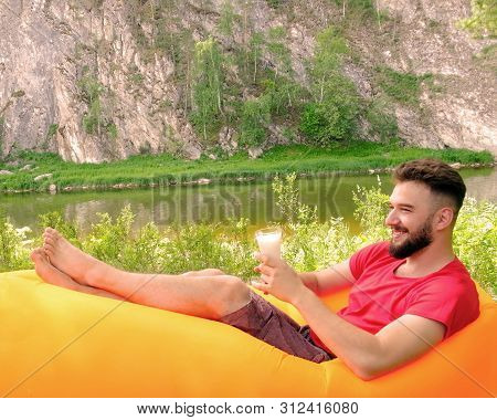A Happy Guy With A Beard In A Red T-shirt Lies On An Orange Inflatable Sofa Lamzac And Holds A Glass