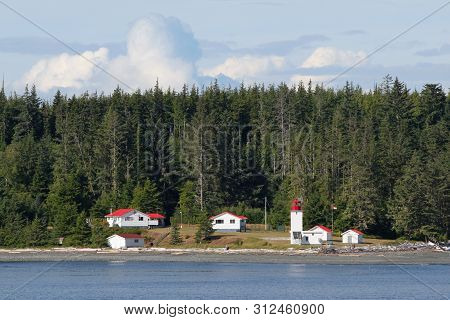 Inside Passage, Canada - August 5, 2006 - Lighthouse And Red-roofed Buildings With Evergreen Forest 