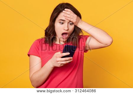 Portrait Of Shocked Emotional Woman Putting One Hand To Forehead, Holding Her Smartphone, Opening He
