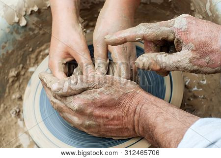 Two Pairs Of Hands Mold Something From Clay On A Potter's Wheel