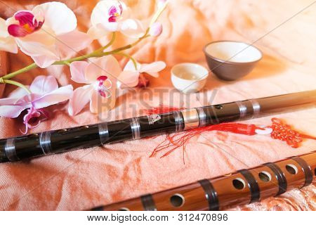 Two Traditional Chinese Bamboo Dizi Flutes Made From Wood With Tea Cups And Flowers In The Backgroun