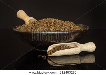 Lot Of Whole Dry Caraway Fruits In A Ceramic Bowl With Two Wooden Scoops Isolated On Black Glass