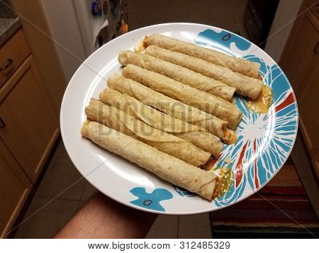 Hand Holding Taquitos On Plate In Kitchen