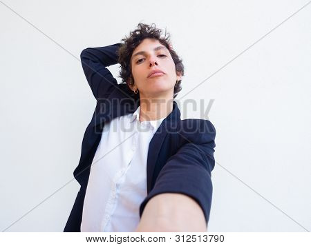 Confident Androgynous Young Woman Holding Cell Phone In Hand And Taking Selfie. Self Portrait Of Fem