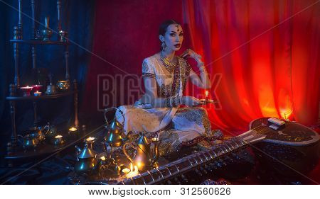 Beautiful Young Indian Woman In Traditional Sari Clothing And Oriental Jewelry With Candle, And The 