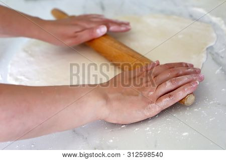 Rolling Pin In Female Hands On A Kitchen, Woman Rolls Out The Dough On A Table. Concept Of Baker, Co