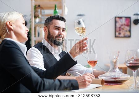 Young successful cavist looking at white wine held by his colleague