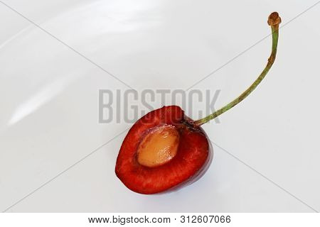 A Half Of A Red Juicy Cherry On A Light Background. Cherrystone. Macro And Highlights. Daylight