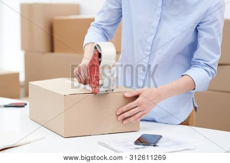 Young female sticking packed order of client with adhesive tape