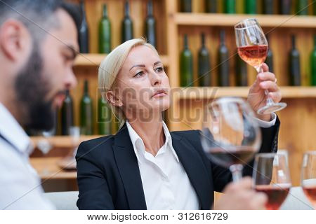 Confident blonde female sommelier or cavist looking at color of wine