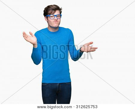Young handsome man wearing blue glasses over isolated background clueless and confused expression with arms and hands raised. Doubt concept.