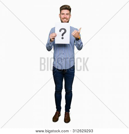 Young handsome man holding paper with question mark happy with big smile doing ok sign, thumb up with fingers, excellent sign
