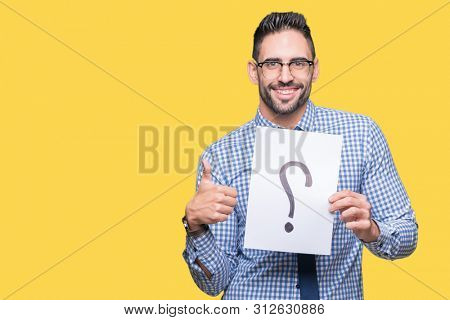 Handsome young business man holding paper with question mark over isolated background happy with big smile doing ok sign, thumb up with fingers, excellent sign