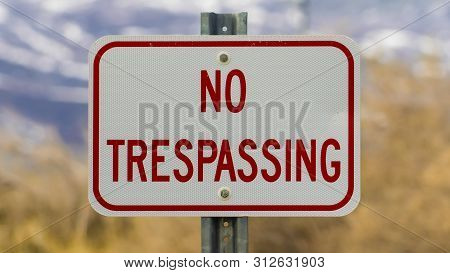 Panorama Frame Close Up Of White Sign Board With The Words No Trespasing Painted In Red Color